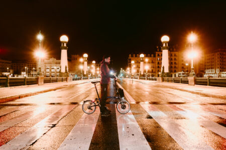 Una persona sujentando una bicicleta en medio de un paso de cebra de la ciudad de noche